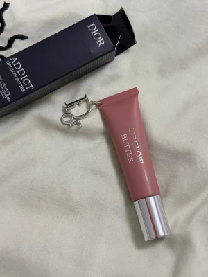 Dior Addict Lip Glow Butter Toffee - Dior Addict Lip Glow Butter i färgen 108 Toffee. Läppbalsamet kommer i en snygg tub med metalliskt lock och har en mjuk, beige-rosa ton. Förpackningen har en elegant Dior-logga och en liten metallring för dekoration. Innehåller 10 ml.