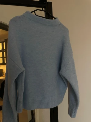 Ljusblå stickad tröja - Mysig ljusblå stickad tröja med avslappnad passform och ribbade muddar vid ärmslut och nederkant. Perfekt för lager på lager och enkel att matcha med jeans eller kjol. Tröjan har en klassisk rund halsringning och är långärmad. (Sticks ej på huden ) 