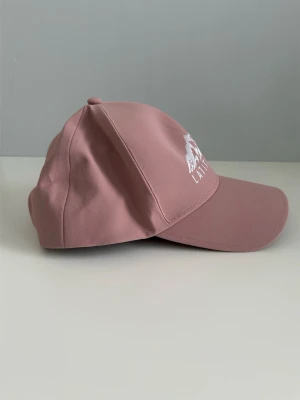 Rosa keps från Latitude 65° - Snygg rosa keps från Latitude 65° med broderad vit logga och bergmotiv framtill. Klassisk böjd skärm och justerbar passform. Perfekt accessoar för en avslappnad och trendig look. Helt NY!