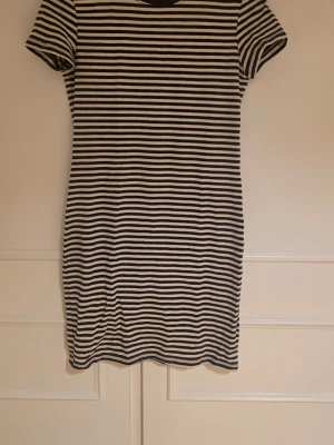 Randig kort klänning i bomull - En enkel och stilren kort klänning med blå och vita horisontella ränder. Klänningen har rund halsringning och korta ärmar.