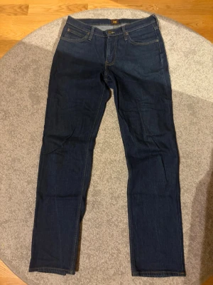 Mörkblå raka jeans från Lee - Snygga mörkblå jeans från Lee med klassisk femficksmodell och raka ben. Jeansen har gul kontrastsöm och Lee-logga på bakfickan. Tillverkade i denim med en stilren look som passar till det mesta.