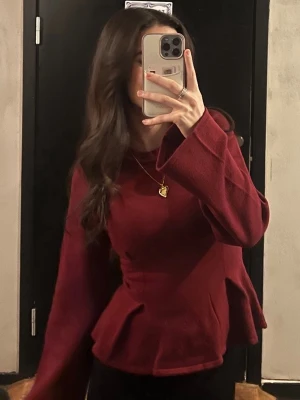 Vinröd tröja Gina Tricot  - Snygg vinröd topp med peplumskärning och vida långa ärmar. Toppen har en figurnära passform upptill och markerad midja. Perfekt att styla med smycken för en trendig look.