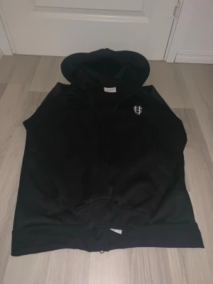 Brazilian tracksuit(zipup) - Snygg svart hoodie från Lindbergh med dragkedja och huva. Klassisk design med liten broderad logga på bröstet. Perfekt för en avslappnad stil. Tillverkad i mjukt material som känns skönt mot huden.