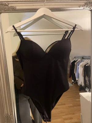 Svart body med dubbla axelband - Snygg svart body med vadderade kupor och dubbla smala axelband. Stilren design i stretchigt material som sitter tajt mot kroppen. Perfekt att styla med jeans eller kjol för en trendig look.