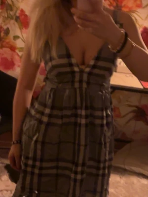 Rutig kortklänning med v-ringning - Supersnygg kortklänning med rutig design i grått, svart och vitt. Djup v-ringning och breda axelband ger en trendig look. Perfekt för dig som vill sticka ut med ett klassiskt men ändå coolt mönster. Klänningen har en avslappnad passform och är lätt att styla.