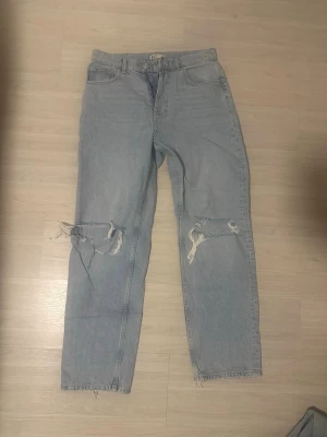 Ljusblå ripped mom jeans - Säljer ett par ljusblå mom jeans med stora slitningar över båda knäna. Jeansen har hög midja, raka ben och klassisk femficksdesign. Perfekta för en avslappnad och trendig streetstyle-look.