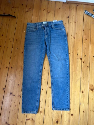 Blå raka jeans med klassisk passform - Säljer ett par blå jeans med rak passform och fem fickor. Från Jack&Jones i storlek 30/32. Jeansen har normal midja och klassiska sömmar, tillverkade i denim. Perfekta för en avslappnad stil och funkar året runt. 