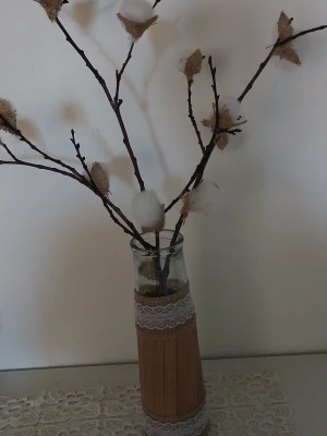 Dekorativ vas med torkade grenar - Säljer en glasvas dekorerad med spets och jute, fylld med torkade grenar och konstgjorda bomullsbollar samt blad i jute. Perfekt som rustik inredningsdetalj till hemmet. Vasen har en naturlig och lantlig känsla och passar bra på bord eller hylla.