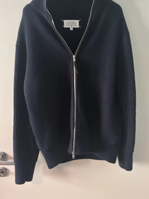 Mörkblå margiela zip  - Köpt för 3000kr på vinted. Mörkblå stickad tröja med dragkedja framtill och hög krage. Tröjan har en ribbad struktur och långa ärmar. Perfekt för lager på lager och har en clean, minimalistisk look.