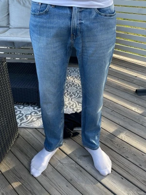 Blå raka jeans med klassisk passform - Säljer ett par blå jeans med rak passform och normal midja. Jeansen har fem fickor, knappgylf och klassiska sömmar. Materialet är denim i bomull och färgen är ljusblå med lätt tvättad look. Perfekta för en avslappnad stil.