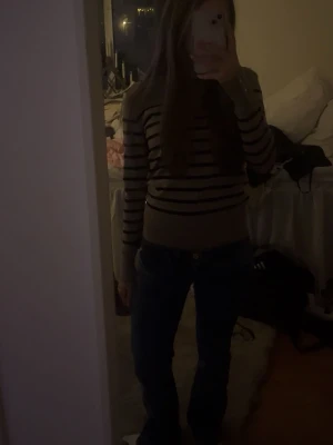 Beige och svart randig tröja - Säljer en beige tröja med svarta ränder. Tröjan har en kroppsnära passform längre ner på tröjan, långa ärmar och rund halsringning. Tröjan har även guldiga knappar längst ut på ärmarna. Perfekt för dig som gillar en enkel men stilren look!