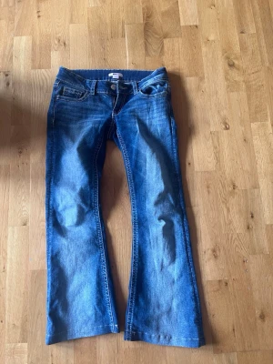 Blå bootcut jeans från Gina Tricot uppfållade till längden 150 - Säljer ett par klassiska blå bootcut jeans från Gina Tricot. Jeansen har fem fickor, normalhög midja och snygga slitningar framtill. Tillverkade i denim med kontrastsömmar och dragkedjegylf. Perfekta för en avslappnad och trendig look.