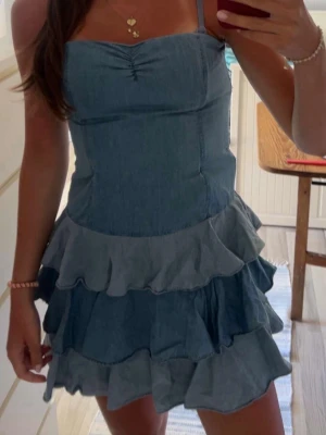  jeansklänning med volanger - Supersöt blå jeansklänning! Klänningen har flera lager volanger i kjolen! Tillverkad i denimtyg som känns både trendigt och bekvämt. Perfekt för dig som gillar en avslappnad men ändå stylish stil.