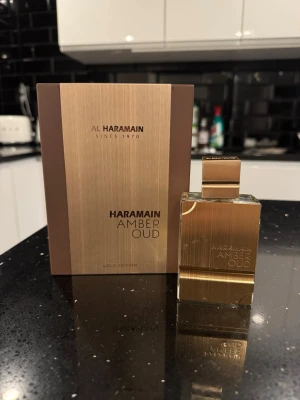 Haramain Amber Oud Gold Edition parfym - Lyxig parfymflaska i guld med matchande ask från Al Haramain. Amber Oud Gold Edition har en elegant, fyrkantig design och metallisk finish. Perfekt för dig som gillar exklusiva dofter och snygg inredningsdetalj på hyllan.