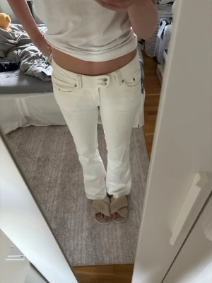 Vita bootcut jeans med broderad ficka - Säljer ett par vita bootcut jeans med snygg broderad detalj på bakfickan och dubbla knappar i midjan. Jeansen har klassisk femficksmodell och är tillverkade i ett stretchigt denimtyg som sitter bekvämt. Perfekta för dig som gillar en clean och fräsch look.