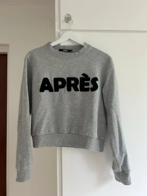 Grå sweatshirt med text från Bik Bok - Grå sweatshirt från Bik Bok med svart, fluffig text 'APRÈS' framtill. Kommer inte till användo!
