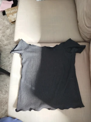 Svart offshoulder topp  - Säljer en svart offshoulder topp från lager 157 i stretchigt material. Toppen har en ribbad struktur och vågig kant nertill för en snygg detalj. Perfekt till jeans eller kjol för en trendig look.