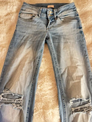 Ljusblå slitna jeans med hål - Säljer ett par ljusblå jeans och hål vid knäna. Materialet är denim med en tvättad look och bootcut. Perfekta för en avslappnad och trendig stil.