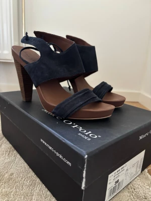Marc O'Polo heels - Snygga marinblåa pumps från Marc O'Polo med bred klack i trälook och öppen häl. Skorna har en bred rem över foten och en smalare framtill, tillverkade i mocka och läder. Perfekta för dig som vill ha både stil och komfort.