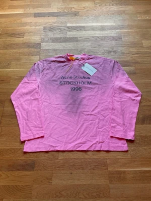 Acne Studios Longsleeve - Säljer en as fet Acne Studios Longsleeve med det klassiska "Acne Studios STOCKHOLM 1996" trycket på bröstet. Tröjans rosa färg samt att den är i Longsleeve-varianten gör att den sticker ut i mangden. Storlek: Small men passar mer som medium. Mått- Längd: 70 cm. Axel till axel: 57 cm. Armhåla till armhåla: 57.5 cm. Skickas inom 24 timmar. Skriv vid funderingar!