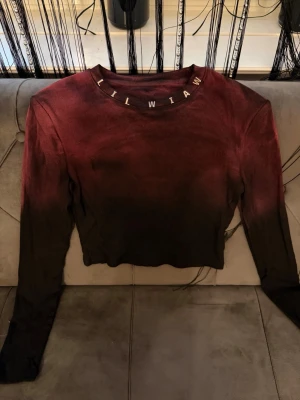 Mörkröd och svart ribbad långärmad topp - Snygg långärmad topp i ribbat material med mörkröd till svart ombre-effekt. Rund halsringning med bokstäver runt kragen som detalj. Croppad passform som ger en trendig look, perfekt till jeans eller kjol.