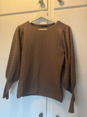 Brun strukturerad tröja från ONLY - Brun tröja från ONLY med vågig struktur och rund halsringning. Tröjan har långa puffärmar med breda muddar.Perfekt för dig som gillar en unik och trendig look.