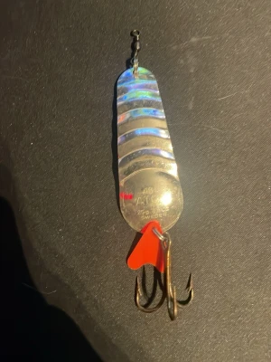 Silverfärgad fiskedrag med trekrok - Säljer ett silverfärgat fiskedrag med holografisk yta och räfflade detaljer. Draget har en trekrok och en liten röd plastdetalj vid kroken. Perfekt för fiskeentusiaster som vill ha ett klassiskt drag i metall. Den e rätt så gammal men aldrig fiskat med