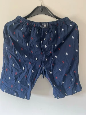 Mörkblå kalsonger Polo Ralph Lauren - Mörkblå kalsonger från Polo Ralph Lauren med elastisk midja och knytband. Tyg med broderade loggor i vitt och rött över hela plagget. Klassisk och bekväm passform, tillverkade i mjuk bomull.