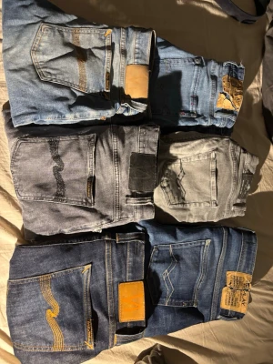 Flera par jeans i olika tvättar - Säljer ett gäng jeans i olika blå och grå tvättar. Några har kontrastsömmar och klassiska bakfickor med broderade detaljer. Passar dig som gillar varierad denimstil och vill ha flera alternativ i garderoben.