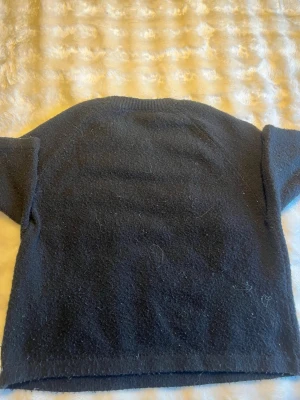 Svart stickad tröja - En enkel och stilren mörkgrå stickad tröja med rund halsringning och långa ärmar. Tröjan har en rak passform och är gjord i ett mjukt, lite luddigt material som känns skönt mot huden. Den är använd och lite nopprig men fortfarande i bra skick. Säljer därför att jag använder den inte längre. Den är i storlek 146/152 men passar mig super som kan bära M i vissa tröjor. Jag skulle säga stor i storleken. Köpt på Ullared! 