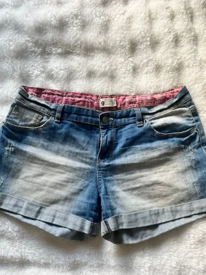Gina tricot - Säljer ett par klassiska blå jeansshorts med snyggt slitna detaljer och uppvikta benslut. Insidan är fodrad med rosa tyg. Säljer därför dem är förstora för mig. Är köpta från Gina för ett bra tag sedan men är knappt använda. Är i storlek 40 och skulle säga att de passar en storlek 40 perfekt!