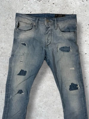 Blå slitna jeans - Säljer ett par ljusblå jeans med slitningar och hål på både fram- och baksida. Jeansen har fem fickor, normal midja och smal passform. Materialet är klassisk denim i bomull och de har en trendig, avslappnad look. Skriv gärna vid funderingar! 😊