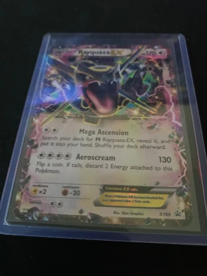 Pokémonkort Rayquaza-EX XY69 - Säljer ett Rayquaza-EX Pokémonkort från XY-serien, nummer 69. Kortet har en holografisk yta och ligger i ett plastfodral. Färgstark design med Rayquaza i centrum och detaljer i guld, grönt och rosa. Perfekt för samlare eller Pokémonfans.