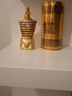 Jean Paul Gaultier Le Male Elixir parfym - Säljer en Jean Paul Gaultier Le Male Elixir parfym i en unik guld- och svart randig flaska formad som en manlig torso. Flaskan är tillverkad i metall och kommer med matchande guldig cylinderförpackning med svarta detaljer.125 ml minst 75-80ml kvar