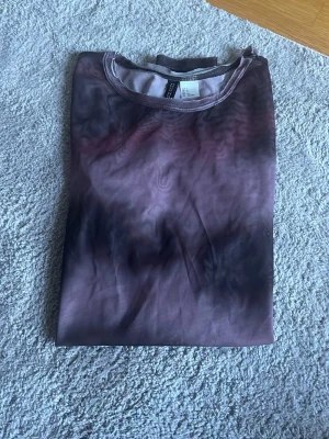 Långärmad mesh topp i lila och svart - Snygg långärmad mesh topp med ett unikt mönster i lila och svart. Tunn och stretchig, perfekt att styla lager på lager eller som statement piece. Rund halsringning och figurnära passform.