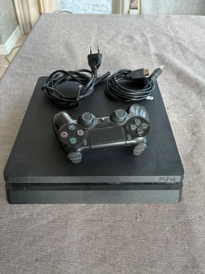 PlayStation 4 Slim med handkontroll - Svart PlayStation 4 Slim med en matchande svart DualShock 4-handkontroll. Konsolen har en stilren, fyrkantig design i matt plast och strömkabel och HDMI-kabel medföljer. Perfekt för gaming och streaming. Rätt så nytt då jag fick dator och det bara står hemma.