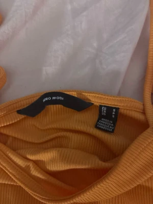 Gul ribbad linnetopp från Vero Moda - Snygg gul ribbad linnetopp från Vero Moda med smala axelband. Perfekt för varma dagar och enkel att matcha med jeans eller kjol. Toppens material är mjukt och stretchigt för en bekväm passform.