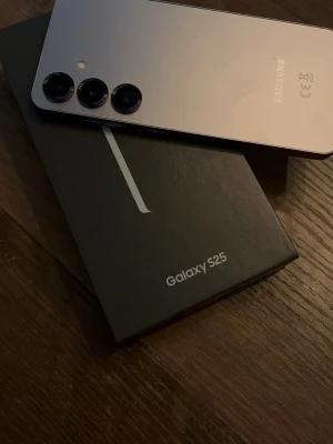 Samsung Galaxy S25 Android mobil - Säljer en Samsung Galaxy S25 i stilren silverfärg. Telefonen har en modern design med rundade hörn, tre bakre kameror och glasbaksida. Kommer med originalkartong. Perfekt för dig som vill ha en kraftfull och snygg Android-telefon.