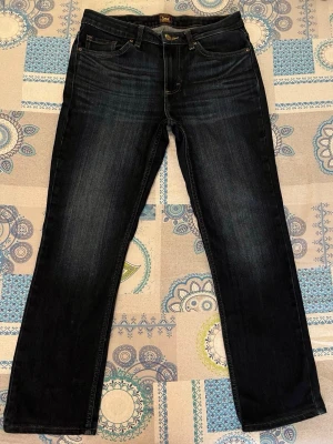 Mörkblå raka jeans från Lee - Snygga mörkblå jeans från Lee med raka ben och klassisk femficksmodell. Jeansen har guldfärgade sömmar och Lee-logga på knappen. Tillverkade i slitstarkt denimtyg som ger en tidlös look.