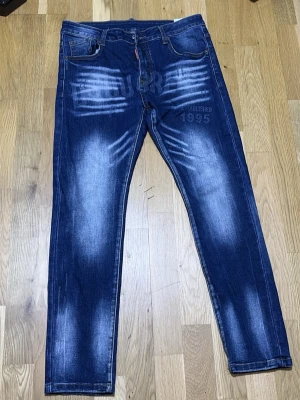 Blå jeans med tryck och slitningar - Säljer ett par blå jeans med tydliga slitningar och tryckdetaljer på både fram- och baksida. Jeansen har raka ben, fem fickor och coola vita effekter på låren. Materialet är klassisk denim och passformen är avslappnad.