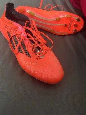 Adidas X Speedflow orange fotbollsskor - Säljer ett par grymma Adidas X Speedflow fotbollsskor i neonorange med svarta detaljer och klassiska tre ränder på sidan. Skorna har låg profil, snörning och dobbar för spel på gräs. Tillverkade i lätt syntetmaterial för maxad speed på planen.