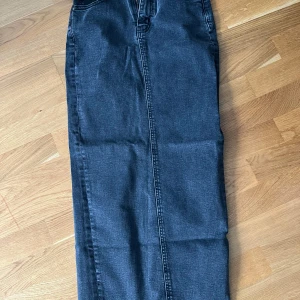 Mörkgrå jeanskjol med slits - Säljer en lång, mörkgrå jeanskjol med klassiska fickor bak och en snygg slits bak. Kjolen har en rak passform och är perfekt för dig som gillar en stilren denimlook.
