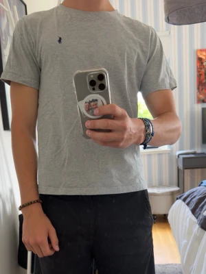 Grå t-shirt från Polo Ralph Lauren - En stilren ljusgrå t-shirt från Polo Ralph Lauren med klassisk passform och korta ärmar. T-shirten har en liten mörkblå logga broderad på bröstet och är gjord i mjuk bomull. Perfekt till jeans eller shorts. Storlek 14-16 160/80