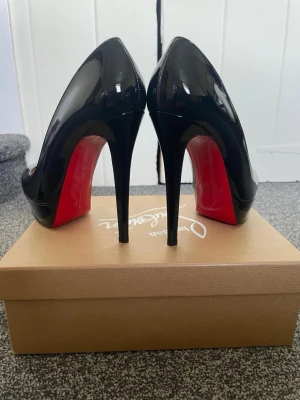 Svarta lackpumps från Louboutin - Säljer ett par ikoniska svarta pumps från Christian Louboutin, modell Bianca 140 i blankt kalvskinn. Skorna har klassisk rund tå, hög platåklack och den signatur-röda sulan. Perfekta för dig som vill sticka ut med lyxig och tidlös stil. Sprillans nya aldrig använda säljer eftersom de inte passade personen, pris ej hugget i sten!