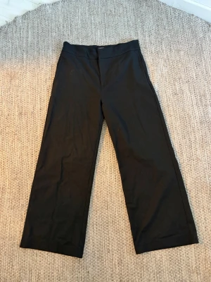 Svarta kostymbyxor från Lindex - Stilrena svarta kostymbyxor från Lindex, modell Lykke. Byxorna har raka ben och hög midja för en klassisk look. Perfekta att matcha med en skjorta eller kavaj, eller t-shirt för en mer avslappnad look.  Materialet känns mjukt och följsamt.