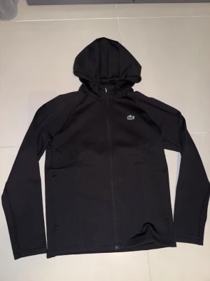 Lacoste zip up hoodie - Helt ny svart lacoste zip up hoodie i storlek S helt oanvänd prislappen sitter kvar 10/10 skick! Köpt för 1400.