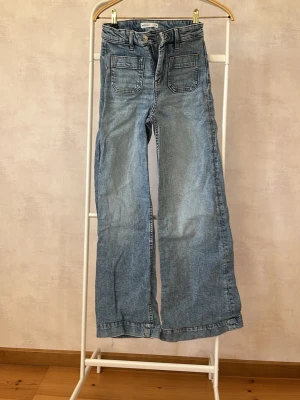 Ljusblå wide leg jeans med fickor - Säljer ett par ljusblå jeans från Gina tricot med raka, vida ben och stora fyrkantiga framfickor. Jeansen har hög midja, bälteshällor och klassisk knappgylf. Materialet är mjuk denim i bomull. Perfekta för en avslappnad och trendig look.