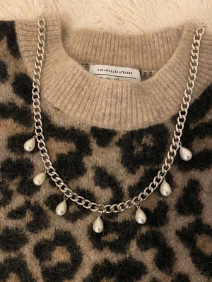 Silverfärgat halsband med pärldroppar - Snyggt halsband i silverfärgad rostfritt stål med sju droppformade vita pärlor som hänger längs kedjan. Perfekt accessoar för att lyfta din outfit med en trendig och elegant touch. Kedjan har en klassisk design och pärlorna ger en cool kontrast.