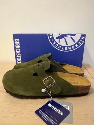  Birkenstock Boston  - Säljer ett par  Birkenstock Boston tofflor i mocka med klassisk korksula och justerbart spänne i metall. Tofflorna har en mjuk innersula och tidlös design som passar perfekt till avslappnade outfits. Perfekta för dig som gillar stilren komfort.