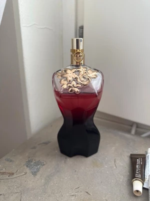 Jean Paul Gaultier Divine parfym - Snygg parfymflaska från Jean Paul Gaultier i form av en kvinnokropp. Flaskan är röd och svart med guldfärgade detaljer och blommönster upptill. Perfekt som statement på sminkbordet och doftar lyxigt.